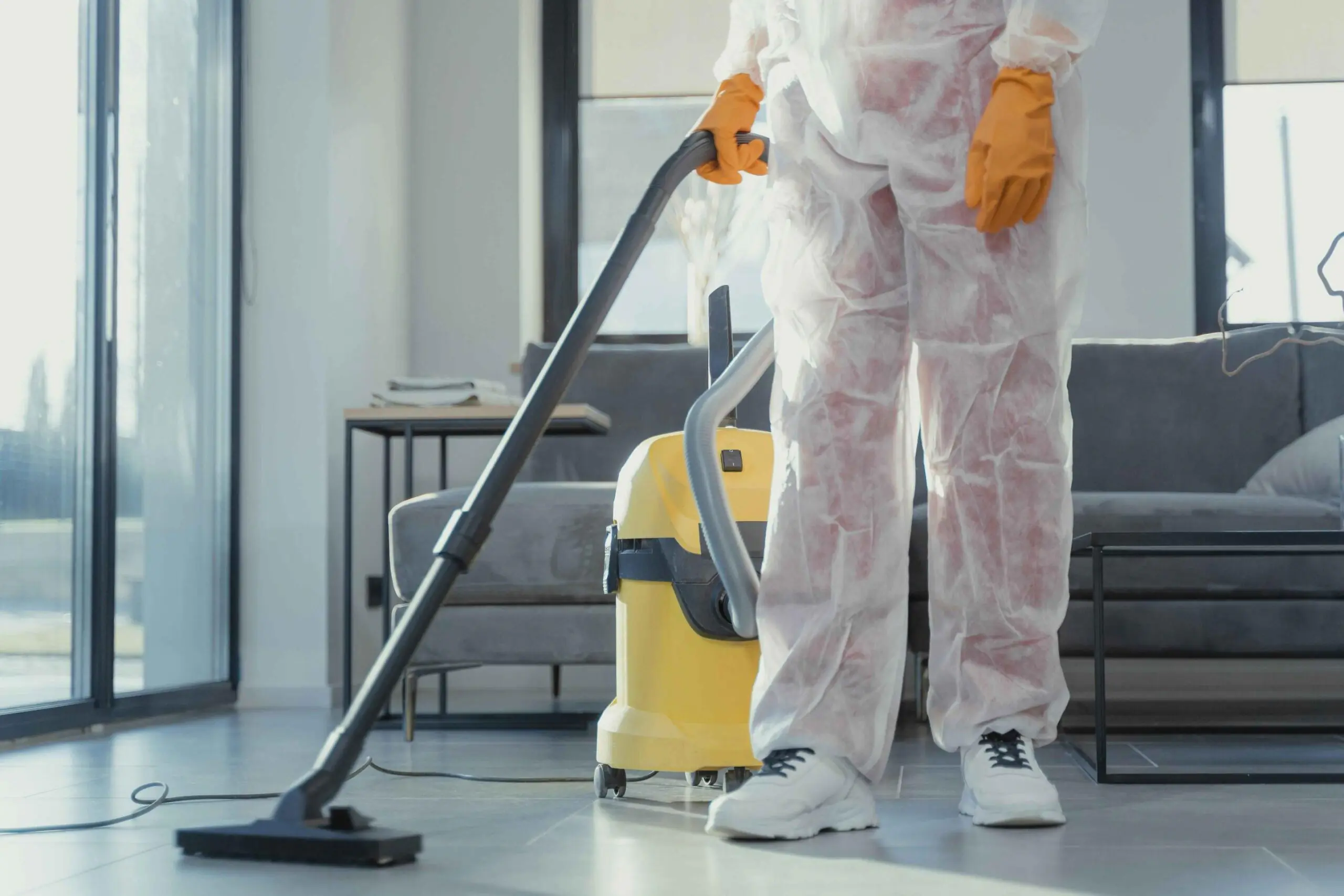 Arborist professional in protective gear using a vacuum cleaner for tree debris cleanup indoors, ensuring a clean and safe environment.
