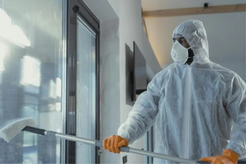 Arborist Services: Worker in protective suit cleaning a tall window with a squeegee, ensuring safety and cleanliness.