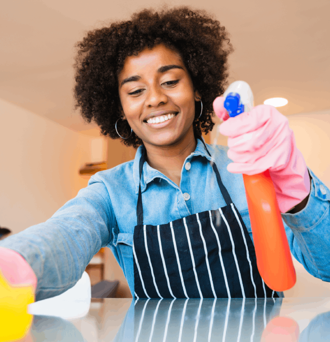 Smiling woman cleaning countertop with spray bottle and sponge. Home cleaning services, professional cleaner.