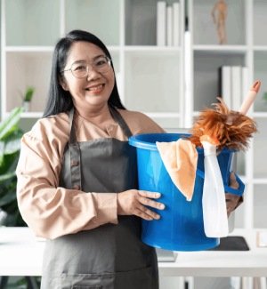 Smiling woman with cleaning bucket, spray bottle, and duster. Professional cleaning service, maid, housekeeping concept.